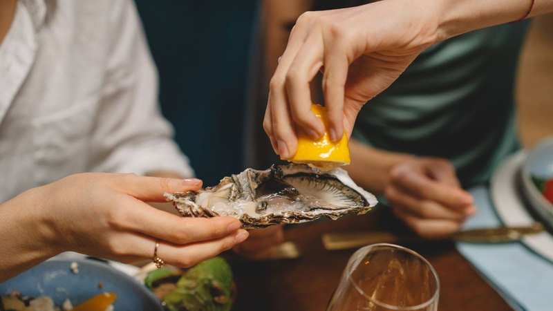 woman squeezing a lemon on an oyster, from the Villa Pereire wine blog on how to pair wine with oysters